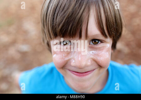 Close up of a cute, smiling young boy with sunscreen on his face, sun protection Stock Photo