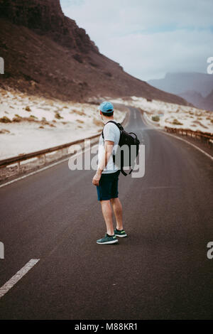 Traveler with backpack standing in the center of an epic winding road. Huge volcanic mountains in the distance behind him. Sao Vicente Cape Verde Stock Photo