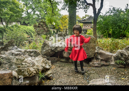 Small girl in red dress dancing in the rain, Liu Yuan Classical Garden, Souzhou, China Stock Photo