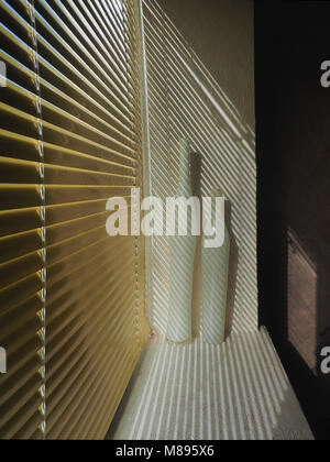 Golden metal blinds, in the white aperture of the window there are 2 porcelain vases, from the blinds the oblique shadows fall, on the right the black Stock Photo
