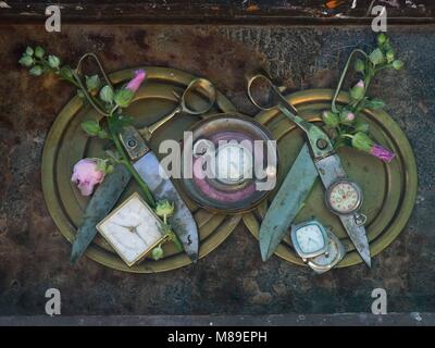 Two pairs of open scissors with rusty blades on copper plates, decorated with pink buds, among white wrist watches. Stock Photo