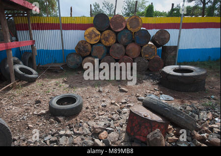 Yard of old gasoline refueling: scattered black rubber tires, garbage, used crushed bottles from under the fuel near the striped fence. Stock Photo