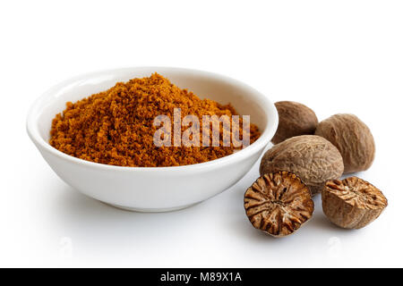 Ground dry mace in white ceramic bowl isolated on white. Whole and halved nutmegs. Stock Photo