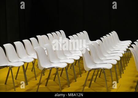 Empty seats in rows audience room white chairs on yellow floor and black wall text space Stock Photo