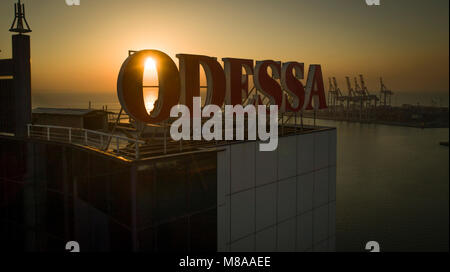 Sun rises behind large Odessa sign on top of the Odessa Hotel, Ukraine. The Black Sea and port are in the background Stock Photo