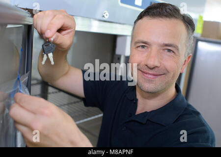 Man by refridgerator holding up set of keys Stock Photo