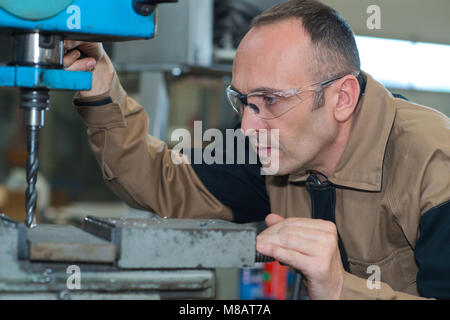 mature man using a drilling machine at industrial factory Stock Photo