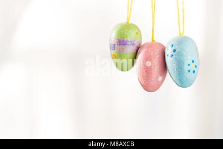 Three decorated Easter Eggs hang from yellow strings. They dangle in front of a white background and leave plenty of copy space. Stock Photo