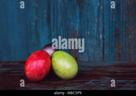 Three colorful handmade easter eggs on blue wooden vintage background. Village life. Christian tradition. Stock Photo