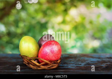 Basket of painted in different colors eggs against the background of green garden on a Sunny day. Easter Breakfast. Easter concept. Traditional decora Stock Photo