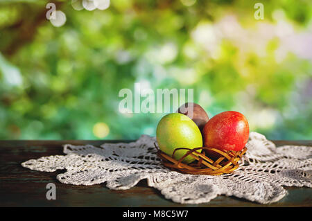 Multicolored, bright Easter eggs in box on a white tablecloth on a wooden old table in the sunlight. a blurred background of nature. Russian village l Stock Photo