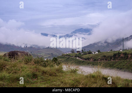 The river Sankosh (Puna Tsang Chu) in early morning mist. Low clouds hang over Himalayas, soft green grassy foreground.  Scenic landscape in Punaka Stock Photo