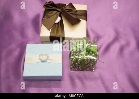 Three white gift boxes with red ribbons form on top of purple background Stock Photo