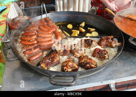 Fast street-food - smoked pork sausages, chicken legs  and stewed cabbage with popato in big frying pan.  Spring sunny fair day outdoor shot Stock Photo