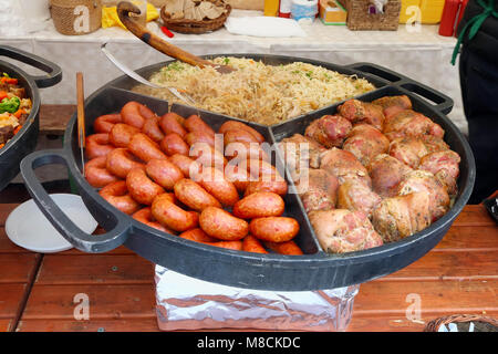 Fast street-food - smoked pork sausages. gammon and stewed cabbage in big frying pan. Sunny spring fair day outdoor shot Stock Photo