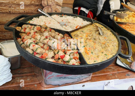 Street fast food -  boiled rice,  beef meat  with vegetables  and fried  smoked pork on wooden skewers  on a big steel  frying pan. Outdoor spring tra Stock Photo
