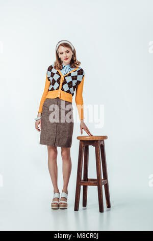 beautiful retro styled girl standing near wooden chair on white Stock Photo