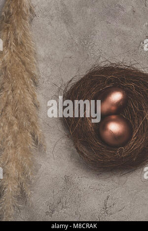 top view of two golden easter eggs in nest on concrete surface  Stock Photo