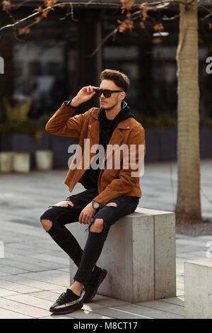 Model looking man sit on the bench in modern park background, look on his watch and around Stock Photo