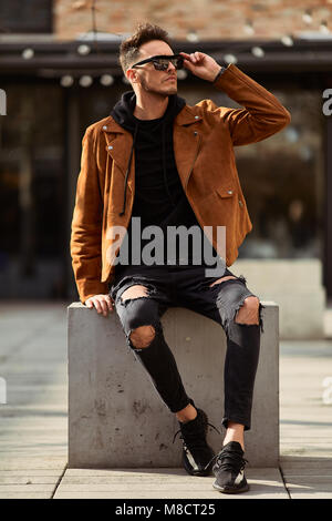 Model looking man sit on the bench in modern park background, look on his watch and around Stock Photo