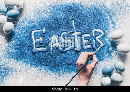 cropped image of woman making easter sign with blue sand on white surface Stock Photo