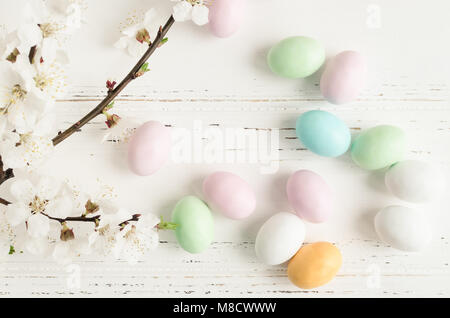 Easter chocolate eggs in pastel colors with branch of spring cherry blossom on white wooden background. Happy Easter Holidays. Top view. Stock Photo