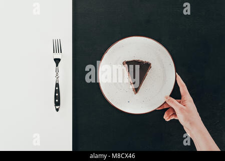 top view of woman holding plate with piece of cake on black background Stock Photo