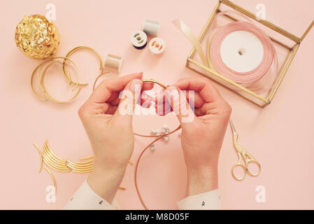 Jewelry designer workplace. Woman hands making handmade jewelry. Freelance fashion femininity workspace in flat lay style. Pastel pink and gold Stock Photo