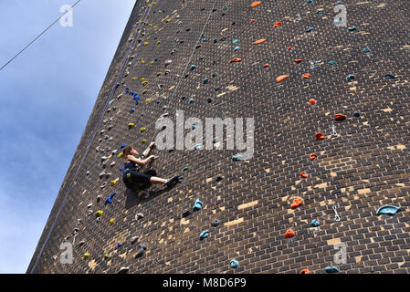 woman climbs up an artificial rock wall - secured with a rope against falling Stock Photo