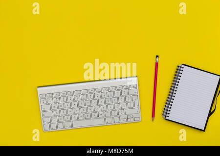 Minimal computer keyboard notebook overhead on bright yellow background Stock Photo