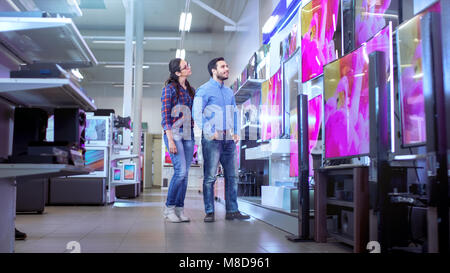 In the Electronics Store Young Couple is Choosing Which a New Model of 4K TV's is Best for Their Home and Budget. Stock Photo