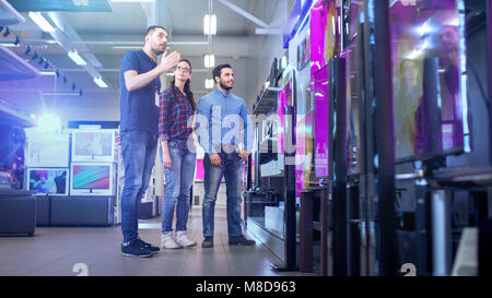 In the Electronics Store Professional Consultant Approaches Young Couple with His Expert Advice on Which of New Models of 4K TV's is Best Stock Photo