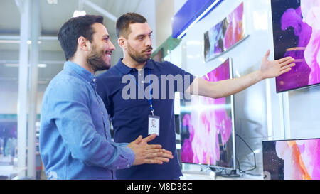 In the Electronics Store Professional Consultant Shows Latest 4K UHD TV's to a Young Man, They Talk about Specifications and What Model is Best