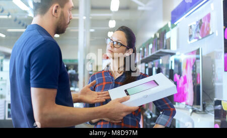 In the Electronics Store Professional Consultant Provides Expert Advice on Tablet Computer Specifications For Beautiful Young Woman. Store is Bright
