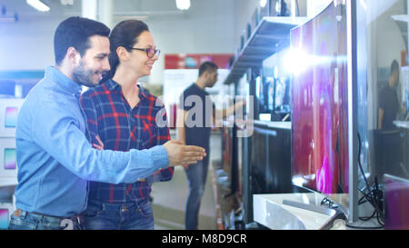 Young Couple Shopping for a New 4K UHD Television Set in the Electronics Store. They're Deciding on the Best Model for Their Happy Family House. Stock Photo