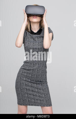 Young blonde woman with VR glasses posing on gray background Stock Photo