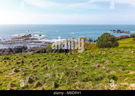 Two people, a man and a woman, looking out to sea at Lizard Point on the Lizard Peninsula, Cornwall, South West England, UK Stock Photo