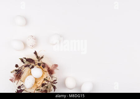 White eggs in stylish straw nest decorated with leaves and feathers surrounded with eggs. Isolated on white background. Flat lay. Easter concept. Stock Photo