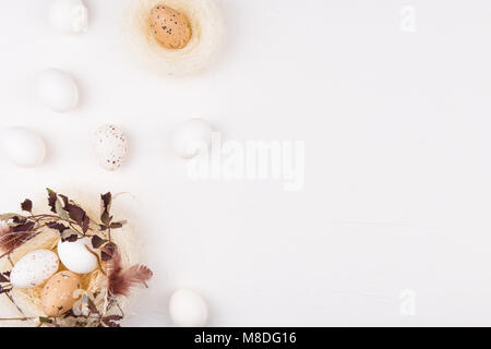 White eggs in stylish straw nest decorated with leaves and feathers surrounded with eggs. Isolated on white background. Flat lay, top view. Easter. Stock Photo