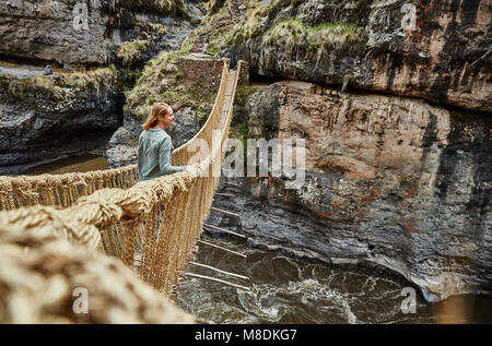 Female tourist looking out from Inca rope bridge, Huinchiri, Cusco, Peru Stock Photo