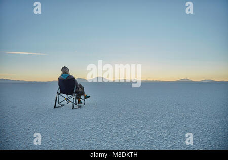 Woman sitting in camping chair, on salt flats, looking at view, Salar de Uyuni, Uyuni, Oruro, Bolivia, South America Stock Photo