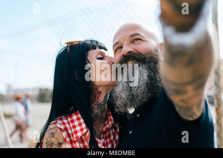 Mature hipster woman kissing boyfriend while taking selfie Stock Photo