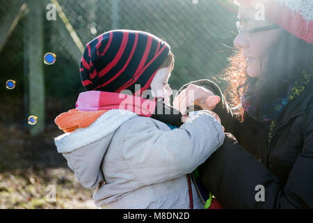 Male toddler and mother blowing bubbles in park Stock Photo
