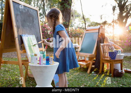Girl and her sister painting on canvas in garden Stock Photo