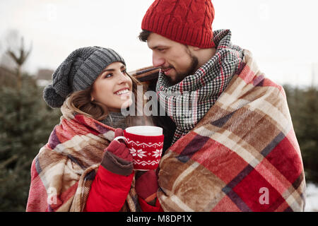 Romantic young couple wrapped in blanket while shopping for christmas tree from forest Stock Photo
