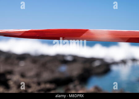 Red tape across the rocks to prevent people going to the shoreline where there are very rough seas breaking over rocks and rockpools on the coast at A Stock Photo