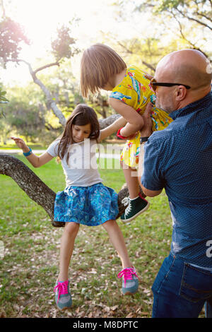 Father and daughters playing outdoors, daughters sitting on tree