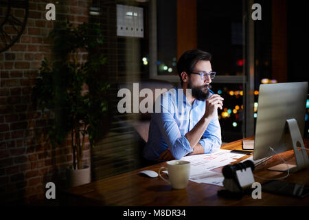 Young businessman looking at computer on office desk at night Stock Photo