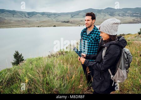 Couple hiking, standing beside Dillon Reservoir, young woman holding digital tablet, Silverthorne, Colorado, USA Stock Photo