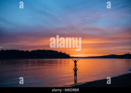 Couple practising yoga on beach at sunset Stock Photo